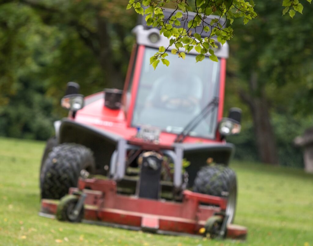 Riding lawn mower collecting fallen leaves in a large yard during autumn, highlighting Gabris Landscaping’s leaf removal services in Springfield, MO.