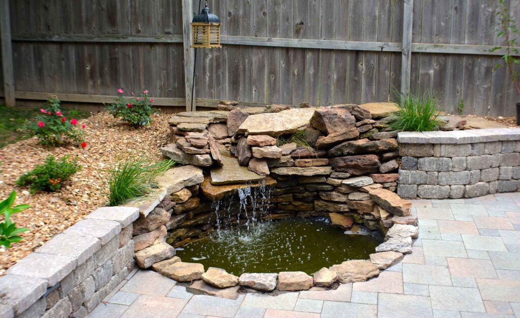 Small backyard stone pond with a waterfall feature and surrounding landscaping.